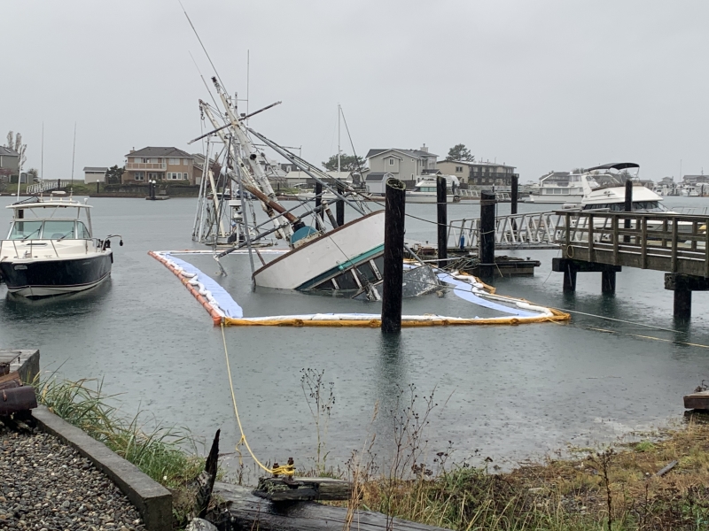 A sunken boat ta a dock surrounded by pollution boom.